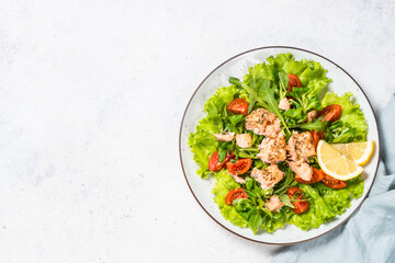 Green salad with baked fish at white table.