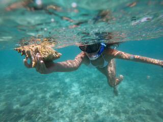 Woman doing snorkeling with mask underwater with seashell. Concept of healthy lifestyle and leisure. Shot taken with underwater camera