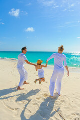 Family at the beach, mother, father and daughter playing on the sand dressed in white tropical outfits