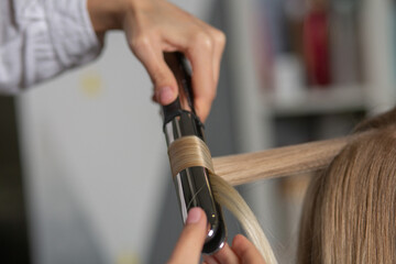 Obraz na płótnie Canvas Hair stylist making curls with styling iron