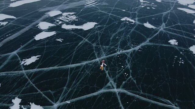 Amazing circular shot from drone of lone person skating on ice. Fantastic natural background of lake surface covered in flat ice with beautiful pattern. Concept of nature, tourism, expedition.