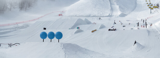 Panoramic view of snowpark with figures for freestyle jumping and jibbing in ski resort