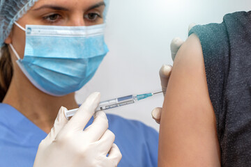 Nurse in surgical mask vaccinating person against viruses