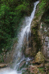From the height of the stream flows clear water-a beautiful waterfall Maiden Tears in Bzyb gorge of Abkhazia. Colorful ribbons hang on the branches of trees - a ritual for good luck