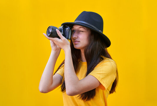 Young girl with hat taking a picture on yellow background