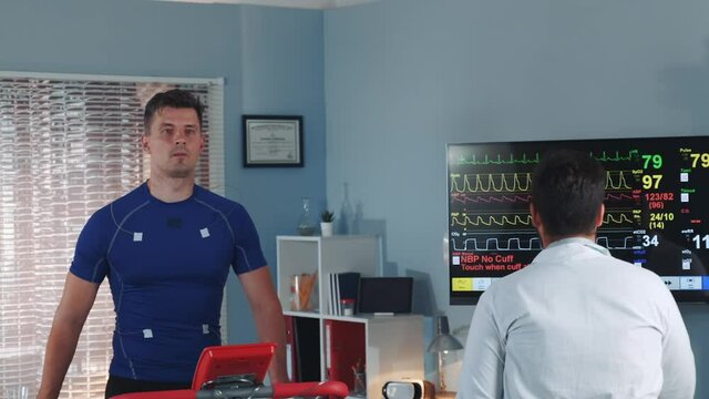 Handsome athlete being tested and monitored by multiracial doctor during treadmill test in lab