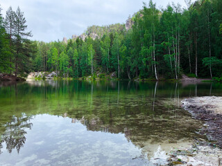 Obraz premium The green forest is reflected in the water. Rock on the lake shore. Summer landscape