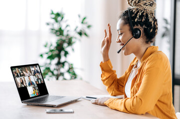 African American female student listens to an online lesson using a laptop and a headset, watches a webinar, studies remotely, the teacher and other students are on the laptop screen. E-learning