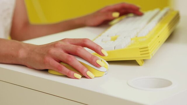 Woman with bright yellow manicure uses yellow computer mouse and keyboard, scrolling wireless mouse, searching some information in the Internet, working in the office, Close up, Slow motion.