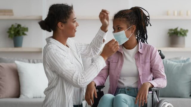 Black Mother Putting Face Mask On Disabled Daughter At Home