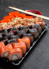 Sushi rolls on a dark stone background with bamboo sticks and soy sauce