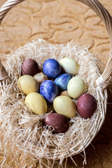 Fototapeta na wymiar Blue, yellow, and brown Easter eggs lie in a wicker basket. The basket is lying on a beige carpet 