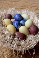 Fototapeta na wymiar Blue, yellow, and brown Easter eggs lie in a wicker basket. The basket is lying on a beige carpet