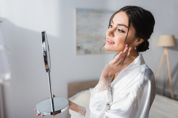pretty bride touching face while looking in mirror in bedroom.