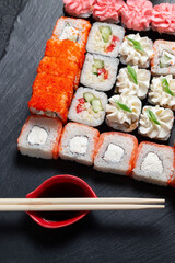 Sushi rolls on a dark stone background with bamboo sticks and soy sauce