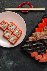 Sushi rolls on a dark stone background with bamboo sticks and soy sauce