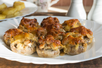 Champignons baked with hard cheese and onions on a white plate on a wooden table. Baked mushrooms with cheese crust close-up.