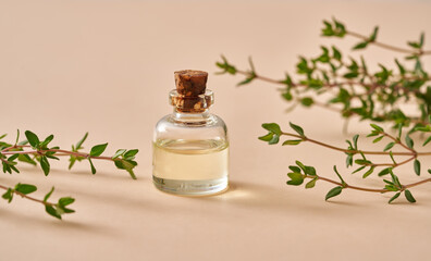 A bottle of essential oil with fresh thyme twigs on pastel orange background