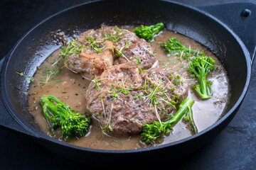 Modern style traditional braised Italian ossobuco alla Milanese with baby broccoli and herb in white wine meat sauce served in a cast-iron design skillet