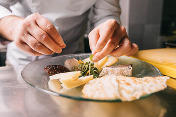 Chef in a restaurant decorate a cheese plate with greens and bread