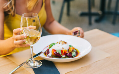 woman eating healthy salad with burrata cheese, arugula salad and tomatoes and holding white wine in a glass