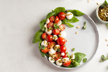 Classic italian caprese salad in grey ceramic plate with fresh tomatoes,mozzarella,basil,pine nuts,pesto and fresh oregano.Foodstyling.Top view with copy space.
