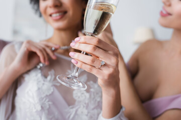 cropped view of african american bride holding champagne glass near bridesmaid on blurred background.