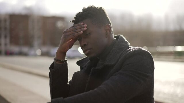 Worried black man suffering alone in emotional pain outside in city sidewalk street