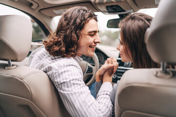 In front of the car, a smiling couple holding hands, looking at each other, luxury car interior