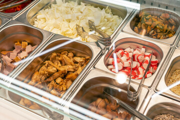 Ready-made ingredients for self-assembly of salads in the store in metal containers with tongs close-up. Self-service in the store