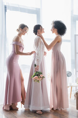 Naklejka premium side view of interracial bridesmaids preparing bride for wedding.
