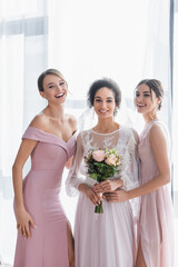 african american woman with wedding bouquet, and cheerful bridesmaids smiling at camera.