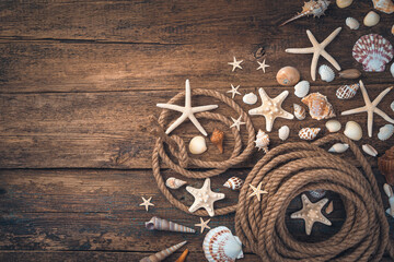 Seashells, starfish of various types and shapes, a rope on a brown wooden background.