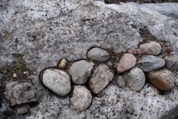 Round white-gray granite stones. Several stones lie on the ground next to each other. Round stones next to the stones are fallen branches and needles that have melted snow.