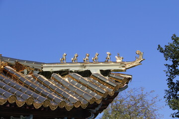 Fototapeta na wymiar Carved animal figures decorating elements of the gilded roof of a Chinese Buddhist temple on a sunny day, against a background of blue sky and trees