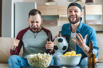 Young excited overjoyed couple of football fans watching play broadcast live on tv celebrating...