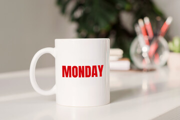 Coffee mug with text MONDAY in workplace background.