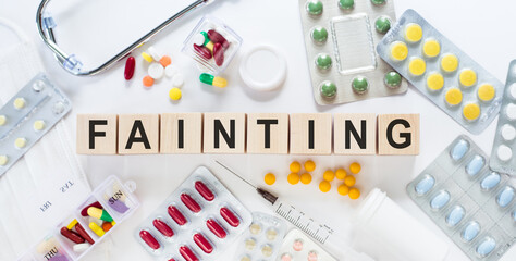 FAINTING medicine word on wooden blocks on a desk. Medical concept with pills, vitamins, stethoscope and syringe on the background.