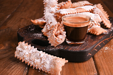 Carnival food TYPICAL and italian espresso. Sfrappole or chiachiere or angel wings and aromatic coffee on a woody background.Traditional sweet crisp pastry deep-fried and sprinkled with powdered sugar