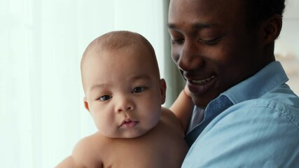 Close up portrait of happy african american father embracing his newborn baby at home, playing and smiling