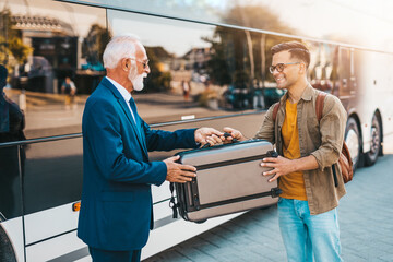 The senior bus driver accepts luggage from passenger.