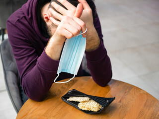 Young male with facial mask is thinking about future. Instant noodles (ramen) in the man wallet as poverty concept. Financial problems, crisis and bankruptcy. Coronavirus and society living issues.