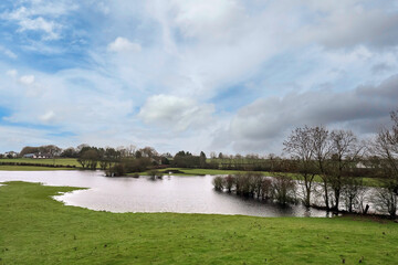 Flooded agriculture land in spring season. Nature seasonal disaster. Green grass field filled with water. Cloudy sky. Nobody.