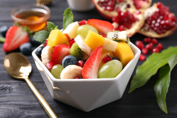 Delicious fresh fruit salad in bowl on black wooden table