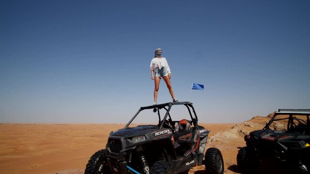Young woman standing on the roof of an offroad sand buggy in the desert