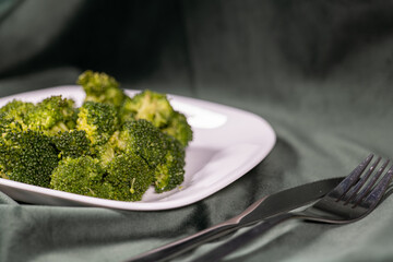 healthy food, boiled broccoli on a white plate on a dark green cloth