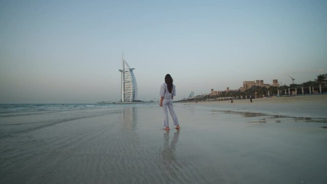 Female tourist standing on the beach and admiring Burj Al Arab hotel in Dubai