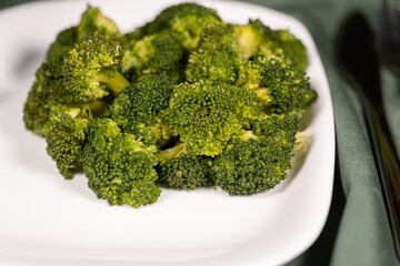 healthy food, boiled broccoli on a white plate on a dark green cloth
