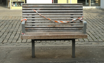 public bench in an empty shopping street with warning tape, business and public life lockdown due to corona virus, symbolic