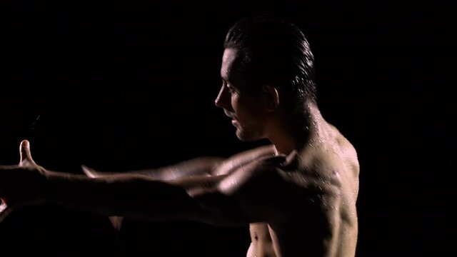 Silhouettes of a sexy man with a naked torso dancing on a black studio background. The dancer's wet body glistens in the rays of light. Night, dancing, romance, passion. Close up. Slow motion.